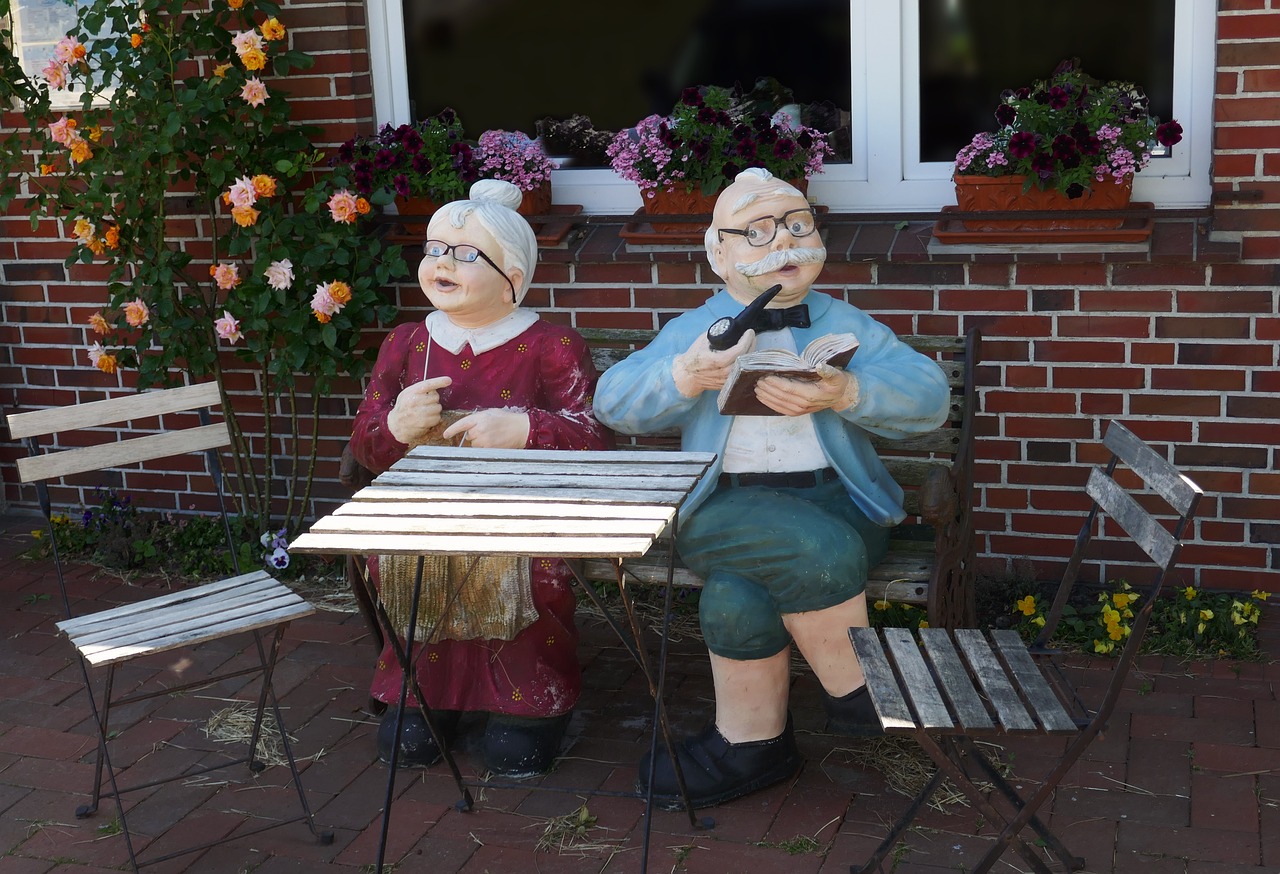 Figuren eines älteren Paares sitzen an einem Tisch vor einem Haus mit Blumen